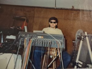 Man with glasses behind sound equipment.