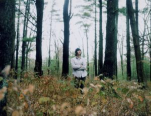 Man with white shirt and cap in the woods.