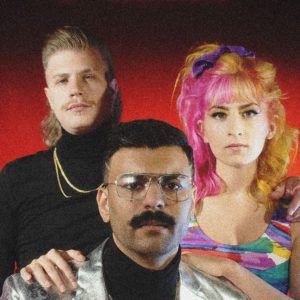 Man in black turtleneck, man in silver jacket with glasses, and women with half pink, half yellow hair.