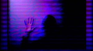 Blurry black and purple picture of a person with hand up.